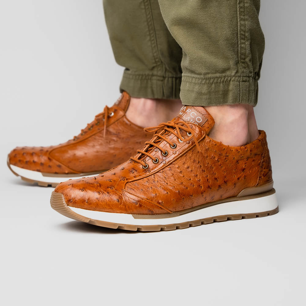 The Scanno Antique Cognac by Marco Di Milano is a brown leather sneaker with an ostrich-patterned, hand-painted finish, white midsole, brown outsole, and brand logo on the tongue—ideal for genuine ostrich quill sneaker fans. Photographed on a plain background.