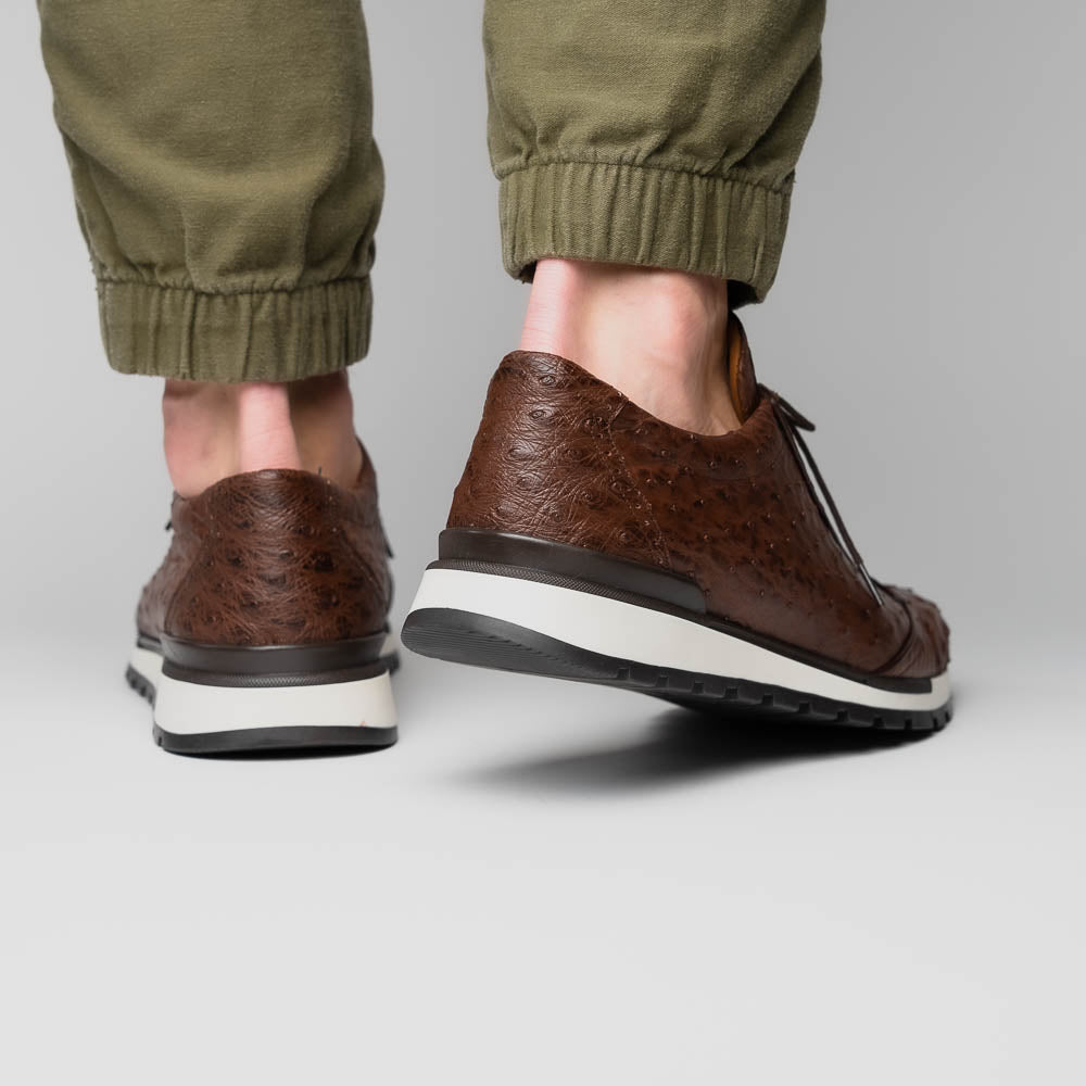 The Scanno Antique Brown sneaker by Marco Di Milano features genuine ostrich quill leather in brown, black laces, and a white-and-black rubber sole. One shoe stands upright while the other rests on its side, highlighting the hand-painted finish.
