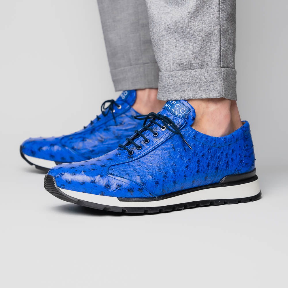 The Scanno Electric Blue sneakers by Marco Di Milano feature textured blue leather, black laces, white soles, and a hand-painted finish—luxury footwear shown upright and leaning to display the black tread.