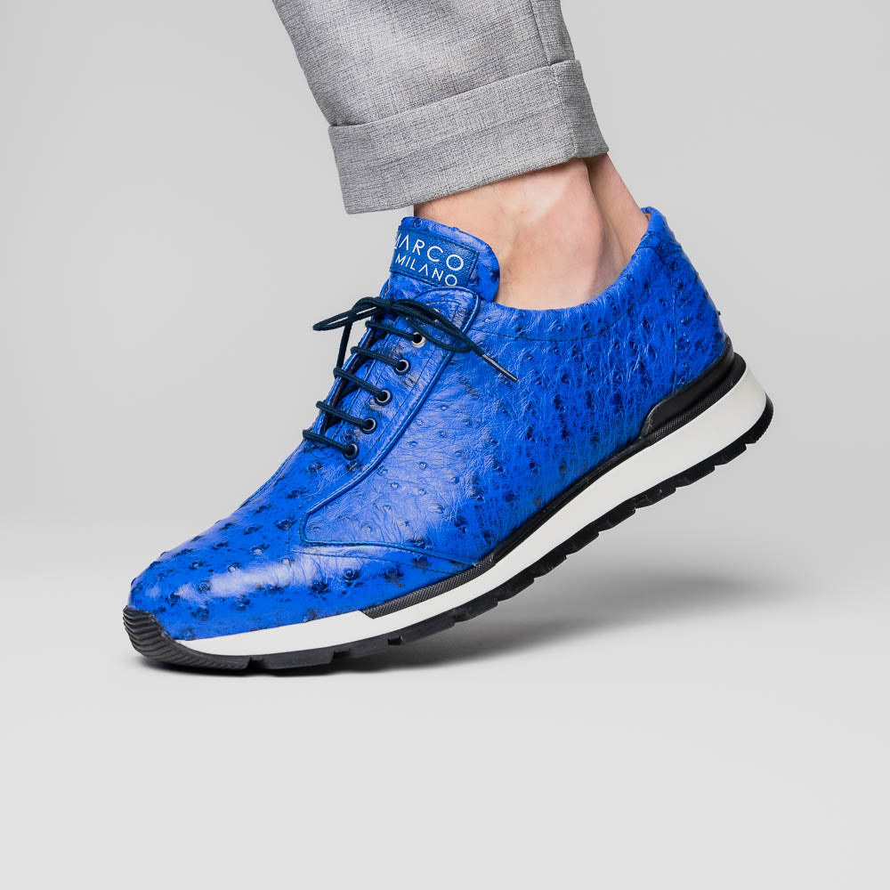 The Scanno Electric Blue sneakers by Marco Di Milano feature textured blue leather, black laces, white soles, and a hand-painted finish—luxury footwear shown upright and leaning to display the black tread.