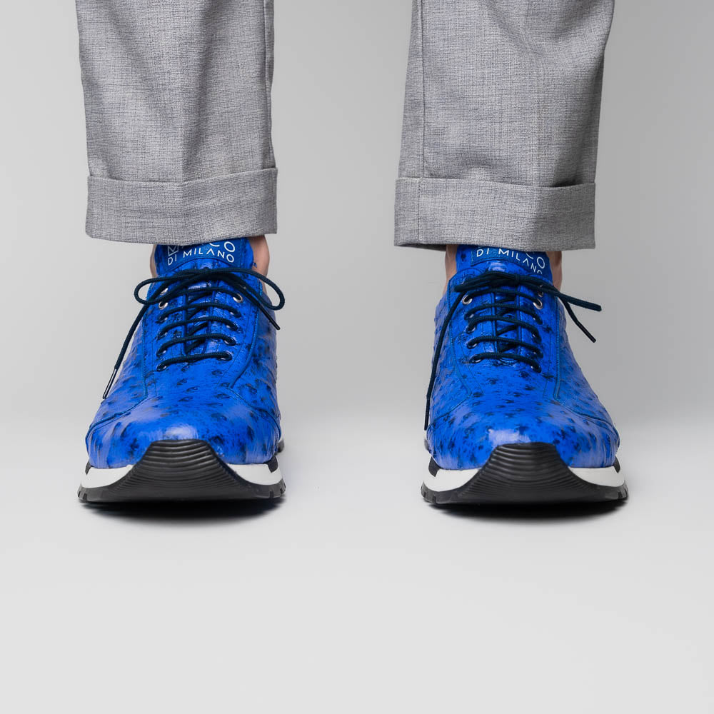 The Scanno Electric Blue sneakers by Marco Di Milano feature textured blue leather, black laces, white soles, and a hand-painted finish—luxury footwear shown upright and leaning to display the black tread.