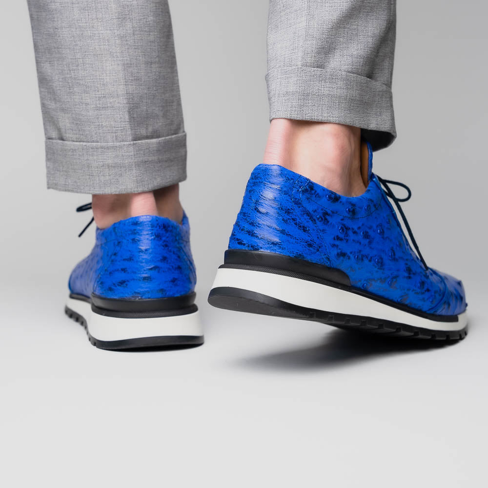 The Scanno Electric Blue sneakers by Marco Di Milano feature textured blue leather, black laces, white soles, and a hand-painted finish—luxury footwear shown upright and leaning to display the black tread.