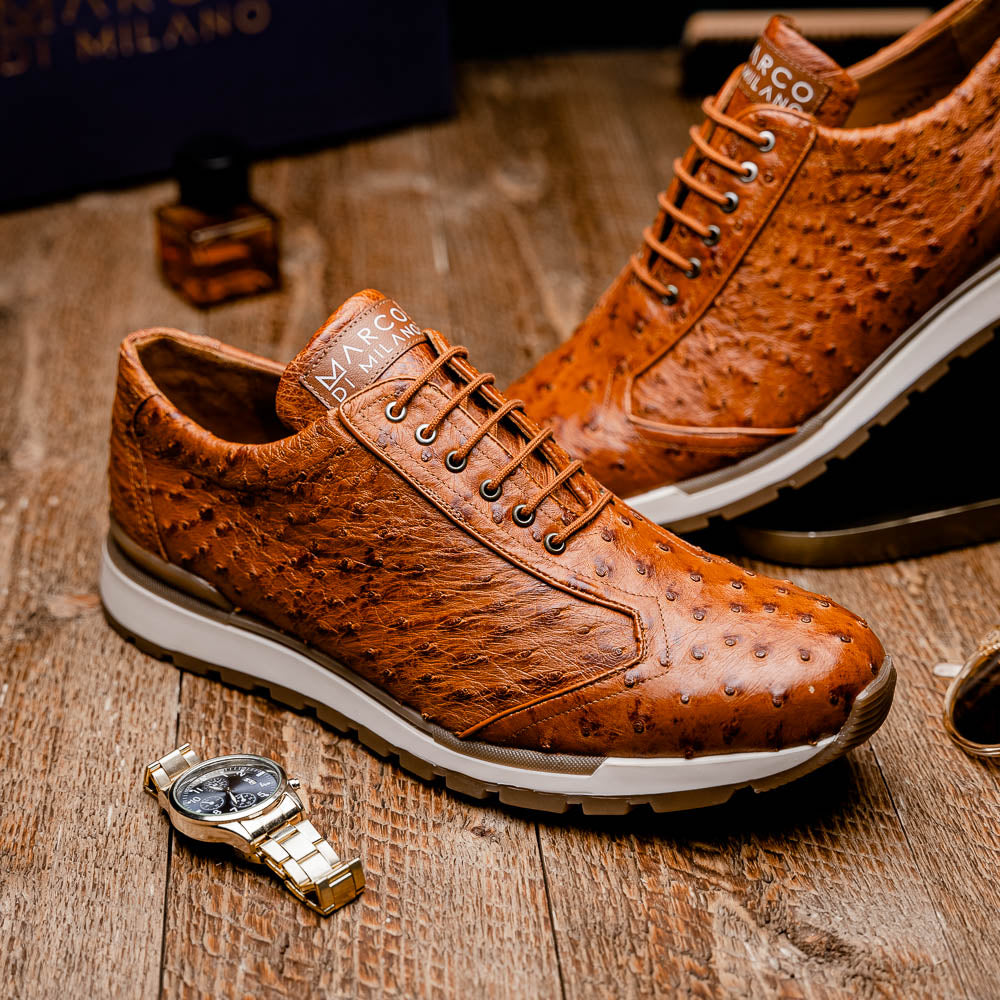 The Scanno Antique Cognac by Marco Di Milano is a brown leather sneaker with an ostrich-patterned, hand-painted finish, white midsole, brown outsole, and brand logo on the tongue—ideal for genuine ostrich quill sneaker fans. Photographed on a plain background.