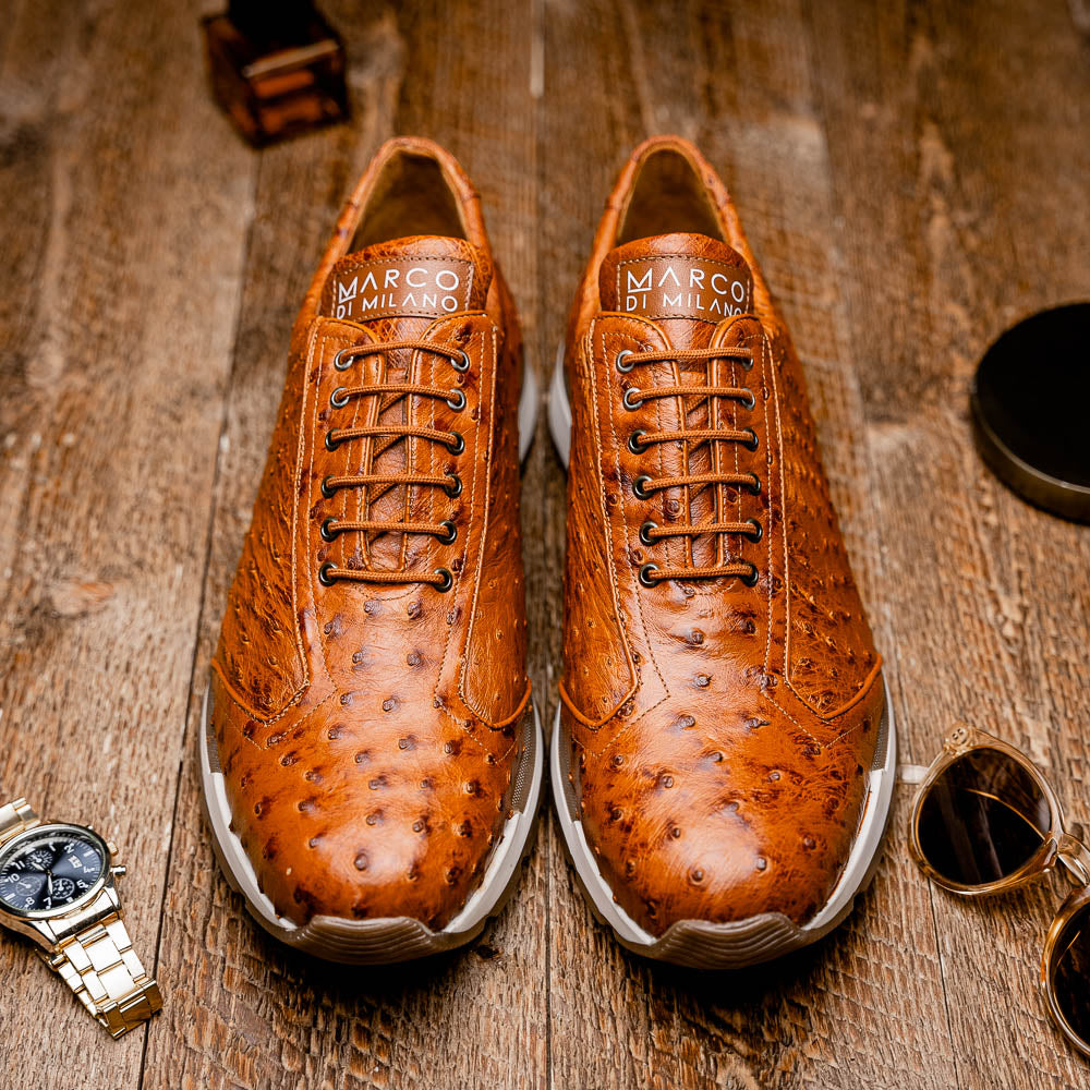 The Scanno Antique Cognac by Marco Di Milano is a brown leather sneaker with an ostrich-patterned, hand-painted finish, white midsole, brown outsole, and brand logo on the tongue—ideal for genuine ostrich quill sneaker fans. Photographed on a plain background.