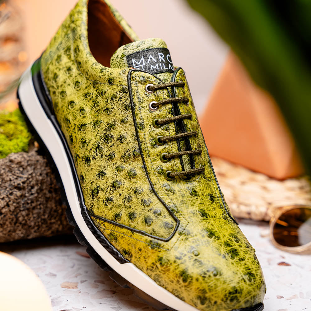 The Marco Di Milano Scanno Antique Green sneakers feature textured genuine ostrich quill in green, black laces, and white soles, with one shoe upright and the other propped beneath—exuding luxury footwear style.