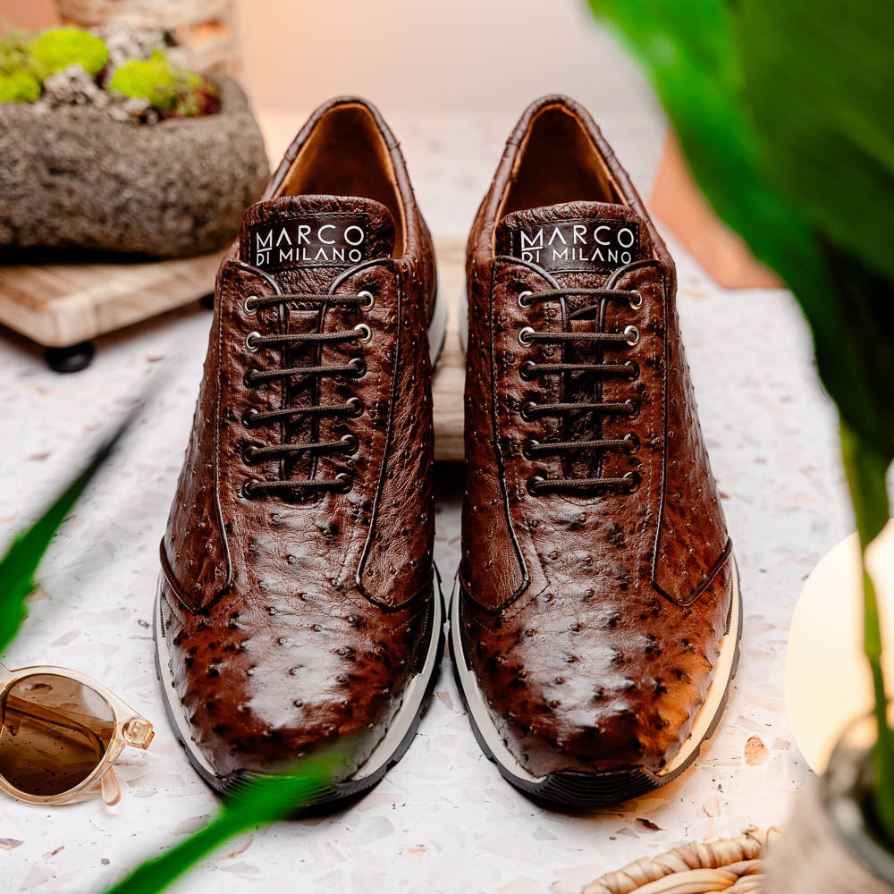 The Scanno Antique Brown sneaker by Marco Di Milano features genuine ostrich quill leather in brown, black laces, and a white-and-black rubber sole. One shoe stands upright while the other rests on its side, highlighting the hand-painted finish.