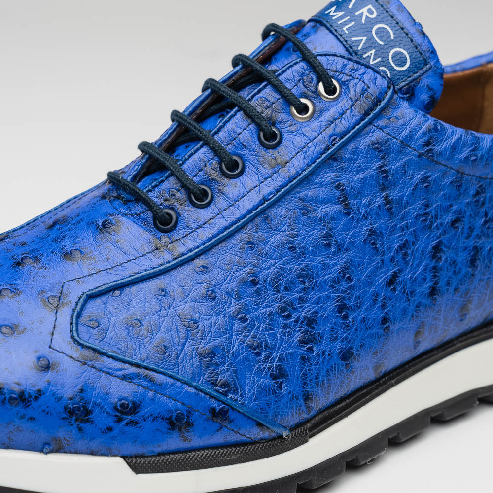 The Scanno Electric Blue sneakers by Marco Di Milano feature textured blue leather, black laces, white soles, and a hand-painted finish—luxury footwear shown upright and leaning to display the black tread.