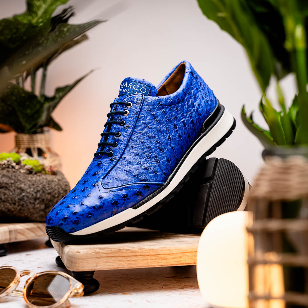 The Scanno Electric Blue sneakers by Marco Di Milano feature textured blue leather, black laces, white soles, and a hand-painted finish—luxury footwear shown upright and leaning to display the black tread.