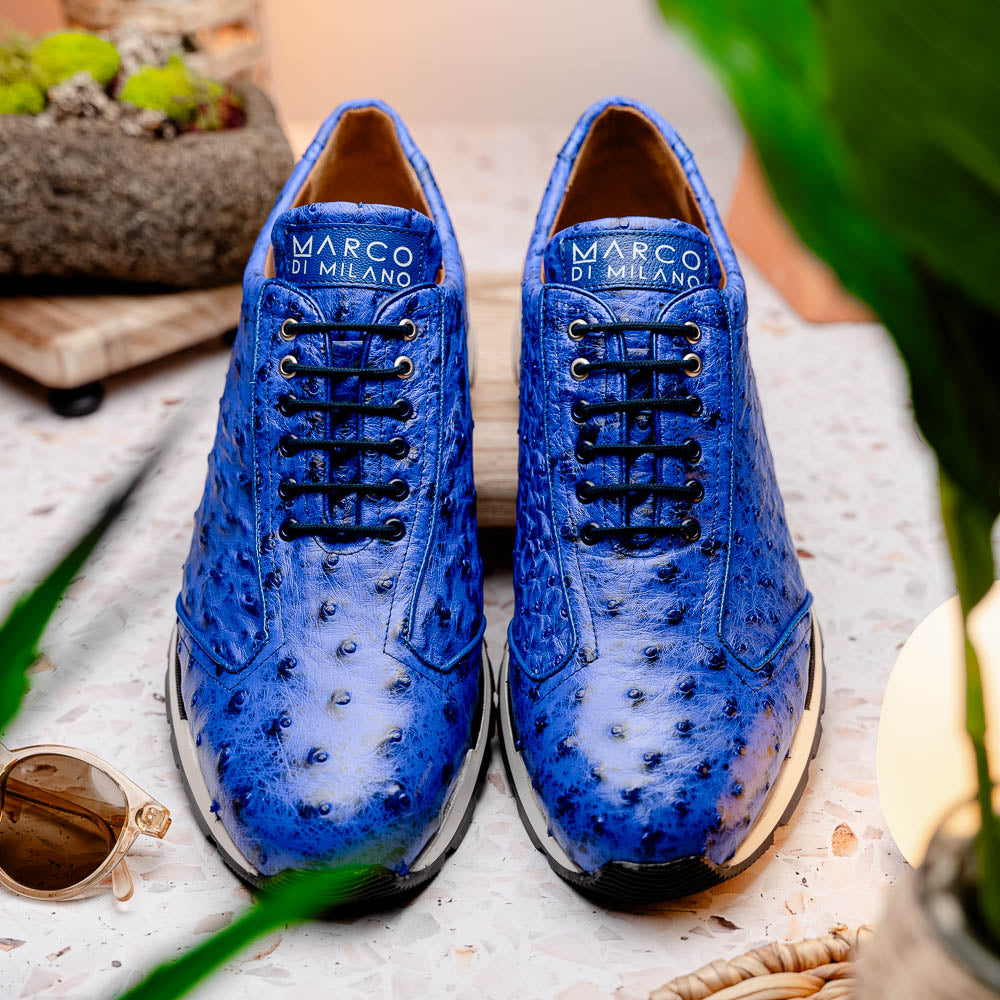 The Scanno Electric Blue sneakers by Marco Di Milano feature textured blue leather, black laces, white soles, and a hand-painted finish—luxury footwear shown upright and leaning to display the black tread.