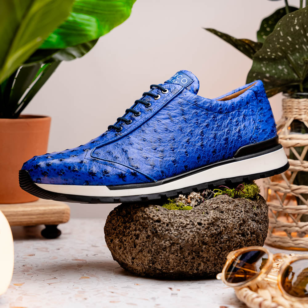 The Scanno Electric Blue sneakers by Marco Di Milano feature textured blue leather, black laces, white soles, and a hand-painted finish—luxury footwear shown upright and leaning to display the black tread.