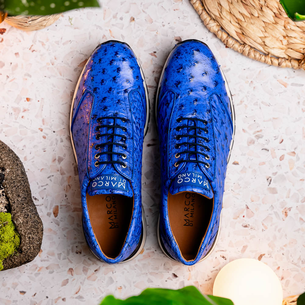 The Scanno Electric Blue sneakers by Marco Di Milano feature textured blue leather, black laces, white soles, and a hand-painted finish—luxury footwear shown upright and leaning to display the black tread.