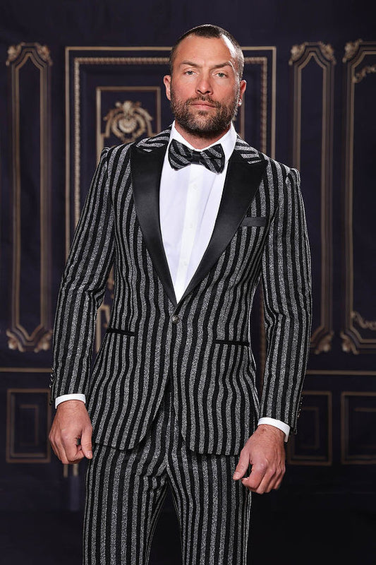 A man wears the MANZINI HEATHER Men's Slim-Fit 2-Piece Glitter Stripe Stage Prom Suit Silver by Manzini with a black bow tie, standing before an ornate, dark backdrop.