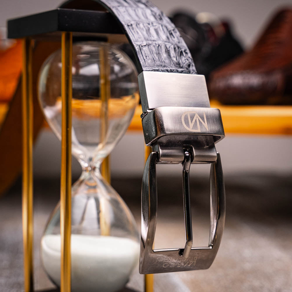 Silvio Belt Black by Marco Di Milano—crafted from black crocodile-embossed leather in the refined style of caiman fuscus-back belts, this belt features meticulous hand-painted finishes and a silver buckle engraved with the Marco Di Milano logo, elegantly coiled on a white background.