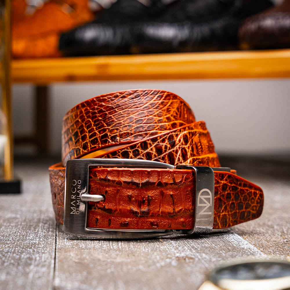 Silvio Belt Rustic Cognac by Marco Di Milano: a brown crocodile-pattern leather belt inspired by caiman fuscus-back, featuring a silver buckle engraved with "MARCO" and "MD"—a signature luxury accessory.