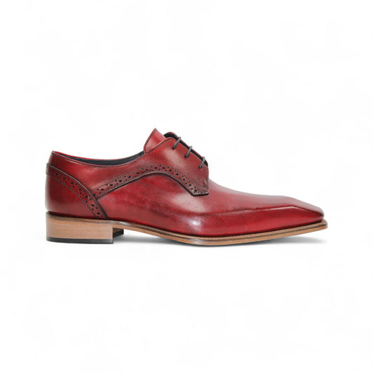 The Duca Di Matiste Duca Spada Antique Red is an Italian leather dress shoe in red with brogue detailing, black laces, and a light brown wooden sole, shown in profile on a white background.