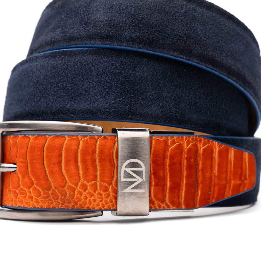 The Hugo Belt Orange / Navy by Marco Di Milano features navy blue ostrich leg suede with an orange textured leather accent near the silver buckle and engraved logos—a stylish match for luxury footwear.