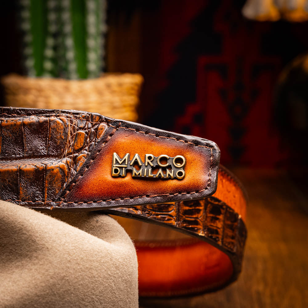 The Texas Belt Aged Brown by Marco Di Milano features embossed brown leather, a brass "MD" logo buckle, inner branding, and design details inspired by the elegance of a caiman crocodile belt.