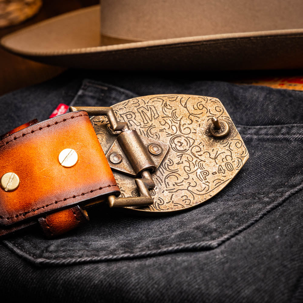 The Texas Belt Aged Brown by Marco Di Milano features embossed brown leather, a brass "MD" logo buckle, inner branding, and design details inspired by the elegance of a caiman crocodile belt.