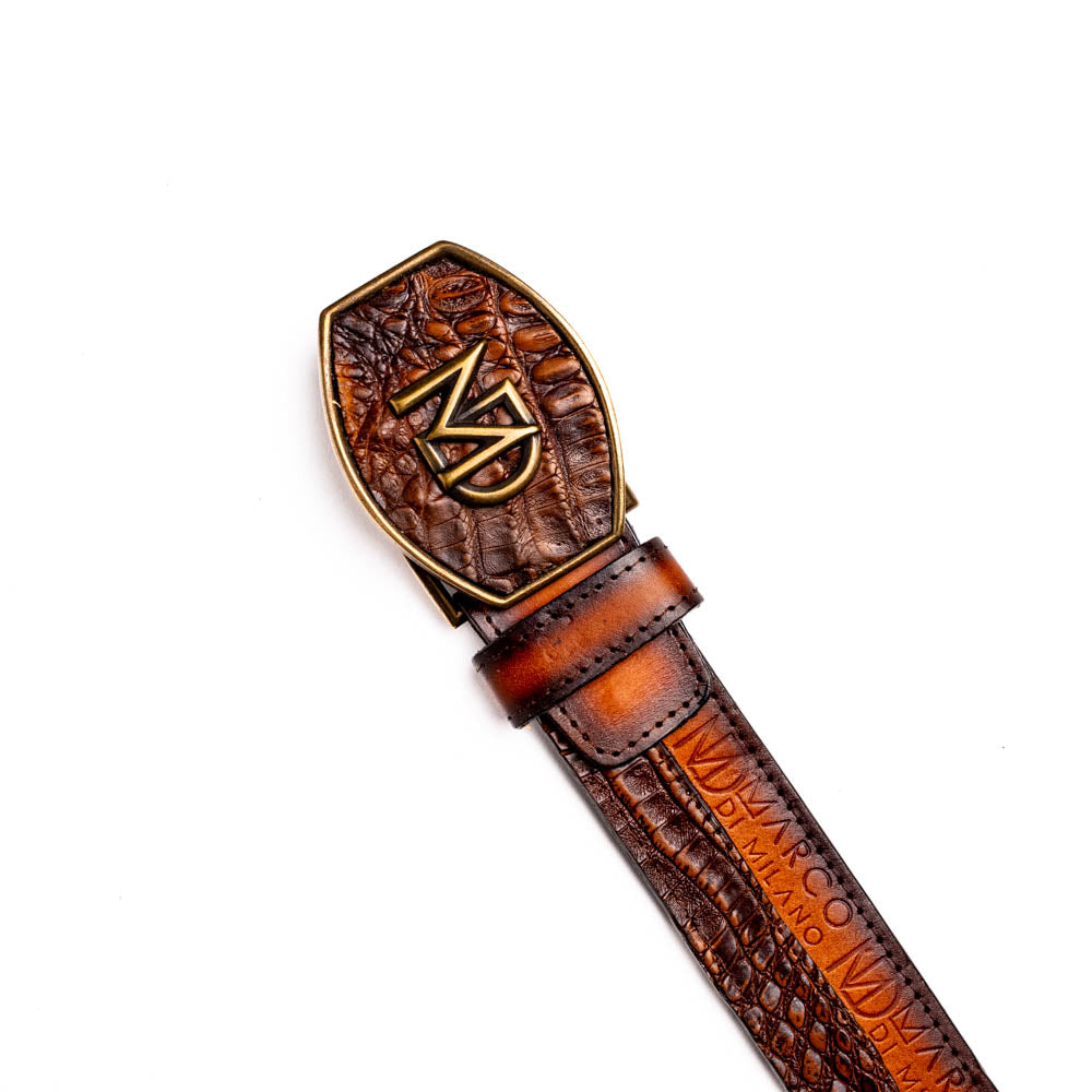 The Texas Belt Aged Brown by Marco Di Milano features embossed brown leather, a brass "MD" logo buckle, inner branding, and design details inspired by the elegance of a caiman crocodile belt.