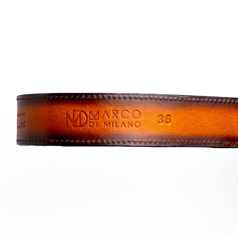 The Texas Belt Aged Brown by Marco Di Milano features embossed brown leather, a brass "MD" logo buckle, inner branding, and design details inspired by the elegance of a caiman crocodile belt.