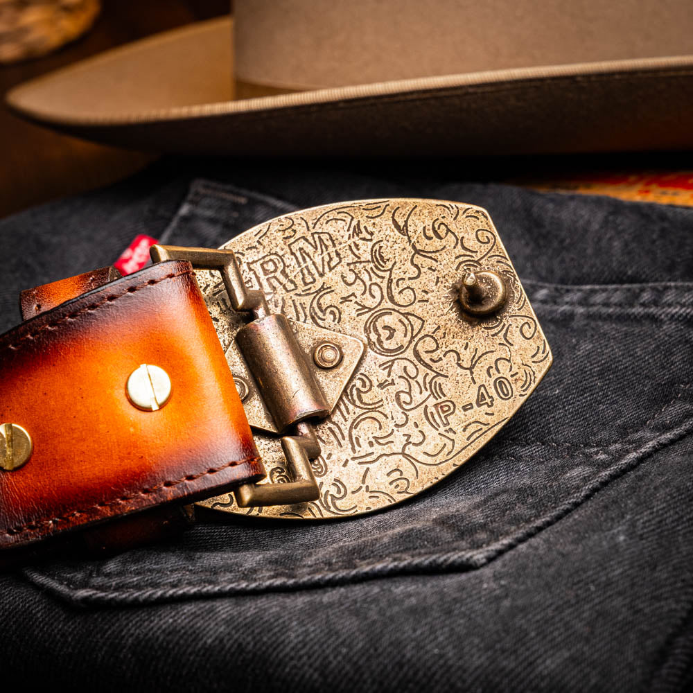 The Texas Belt Aged Maple by Marco Di Milano is crafted from luxurious caiman crocodile skin in a brown finish, featuring a large brass buckle engraved with "MD" and the brand name embossed on the leather.