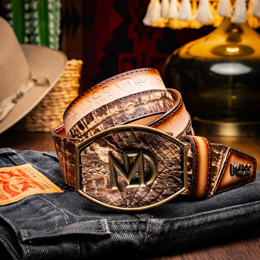 The Texas Belt Stone Brown by Marco Di Milano features embossed brown leather and a large gold-and-brown "CW" buckle, styled after a classic western calfskin belt with "MARCO DI MILANO" branding on the strap.