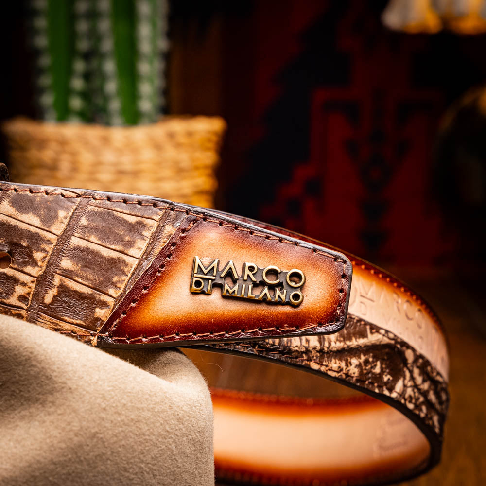 The Texas Belt Stone Brown by Marco Di Milano features embossed brown leather and a large gold-and-brown "CW" buckle, styled after a classic western calfskin belt with "MARCO DI MILANO" branding on the strap.