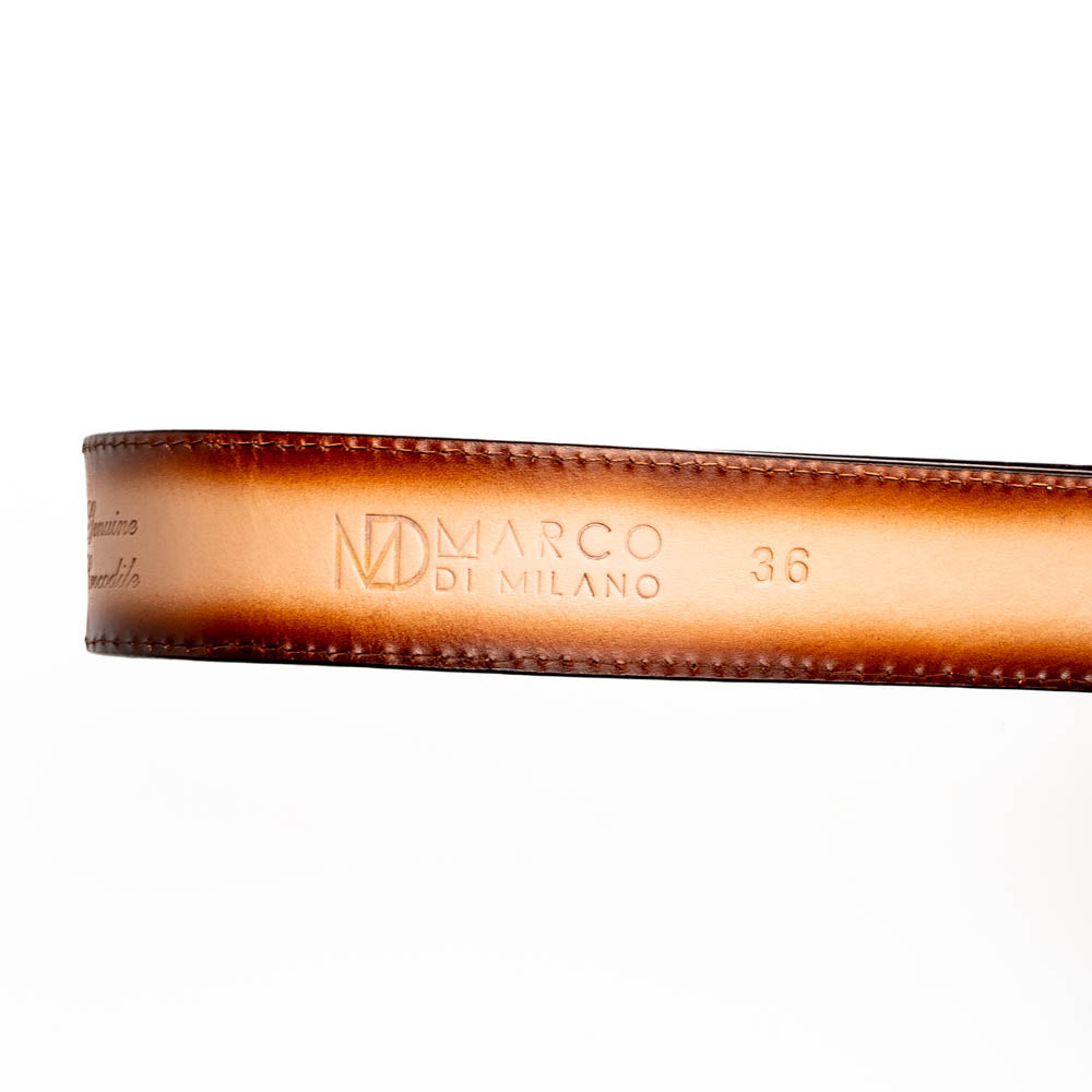 The Texas Belt Stone Brown by Marco Di Milano features embossed brown leather and a large gold-and-brown "CW" buckle, styled after a classic western calfskin belt with "MARCO DI MILANO" branding on the strap.