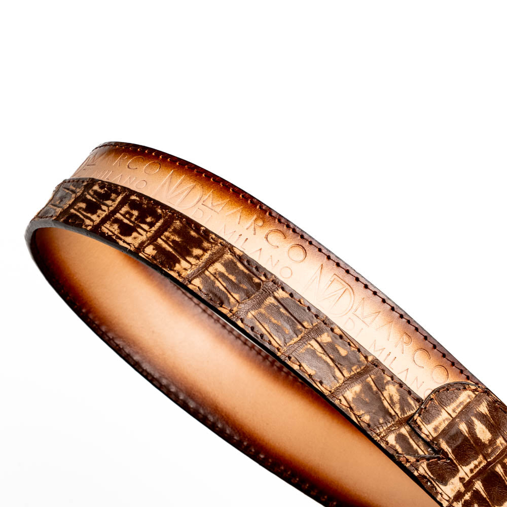 The Texas Belt Stone Brown by Marco Di Milano features embossed brown leather and a large gold-and-brown "CW" buckle, styled after a classic western calfskin belt with "MARCO DI MILANO" branding on the strap.
