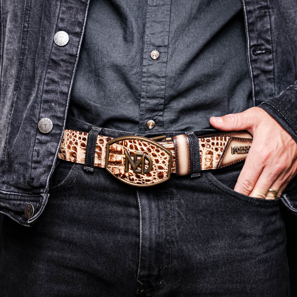The Texas Belt Stone Orix by Marco Di Milano features embossed tan and brown caiman crocodile leather with a large gold and brown MD logo buckle, shown rolled up against a white background.