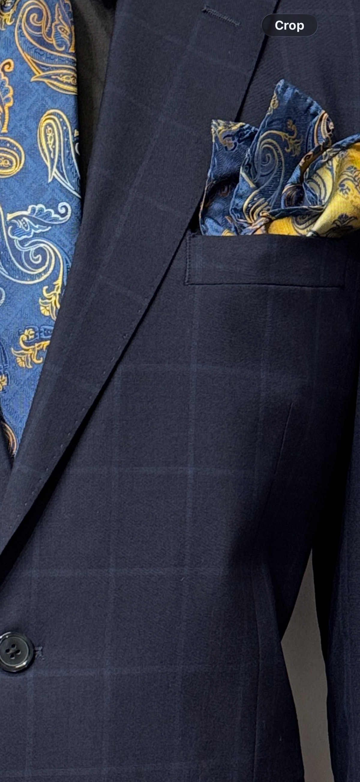 A close-up of the Tiglio Luxe Dolcetto Modern Fit Wool Suit TL7077 showcases a dark navy plaid jacket tailored from pure wool, paired with a blue and gold paisley tie and a matching pocket square in the breast pocket—an elegant expression of luxury menswear from Tiglio Luxe, inspired by the tradition of Italian suits.