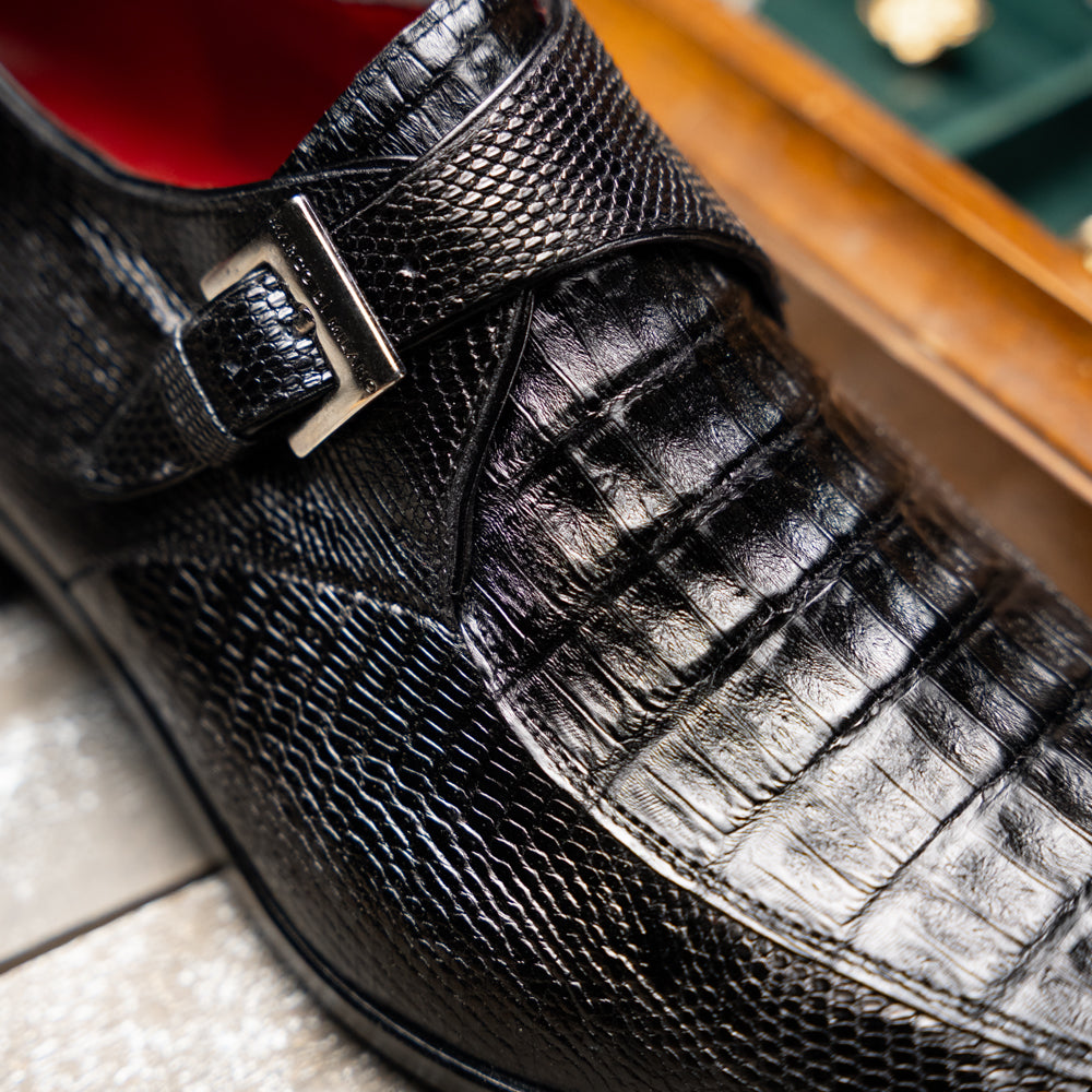 Toluca Black by Marco Di Milano: a black leather dress shoe featuring a crocodile texture and an elegant monk strap side buckle, displayed with one shoe upright and the other revealing its brown leather sole—a refined luxury footwear choice.