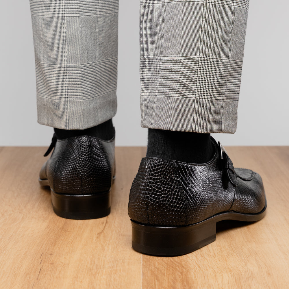 Toluca Black by Marco Di Milano: a black leather dress shoe featuring a crocodile texture and an elegant monk strap side buckle, displayed with one shoe upright and the other revealing its brown leather sole—a refined luxury footwear choice.