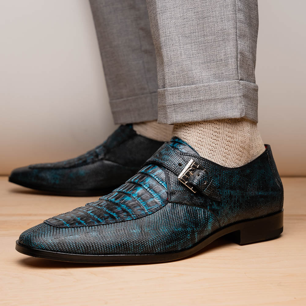 A pair of Toluca Rustic Blue exotic leather dress shoes by Marco Di Milano features a buckle detail, with one shoe on its side showing the tan leather sole and “MARCO DI MILANO” branding.