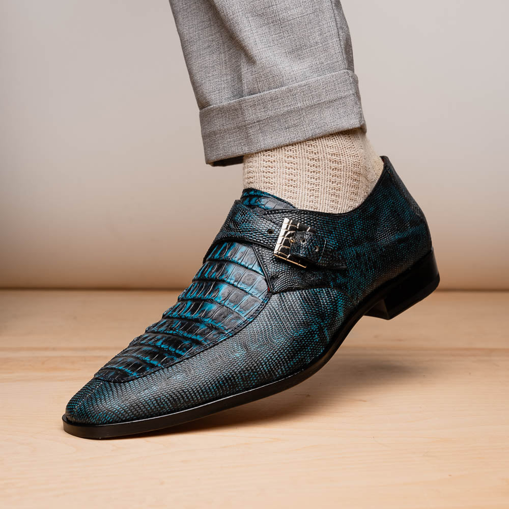 A pair of Toluca Rustic Blue exotic leather dress shoes by Marco Di Milano features a buckle detail, with one shoe on its side showing the tan leather sole and “MARCO DI MILANO” branding.