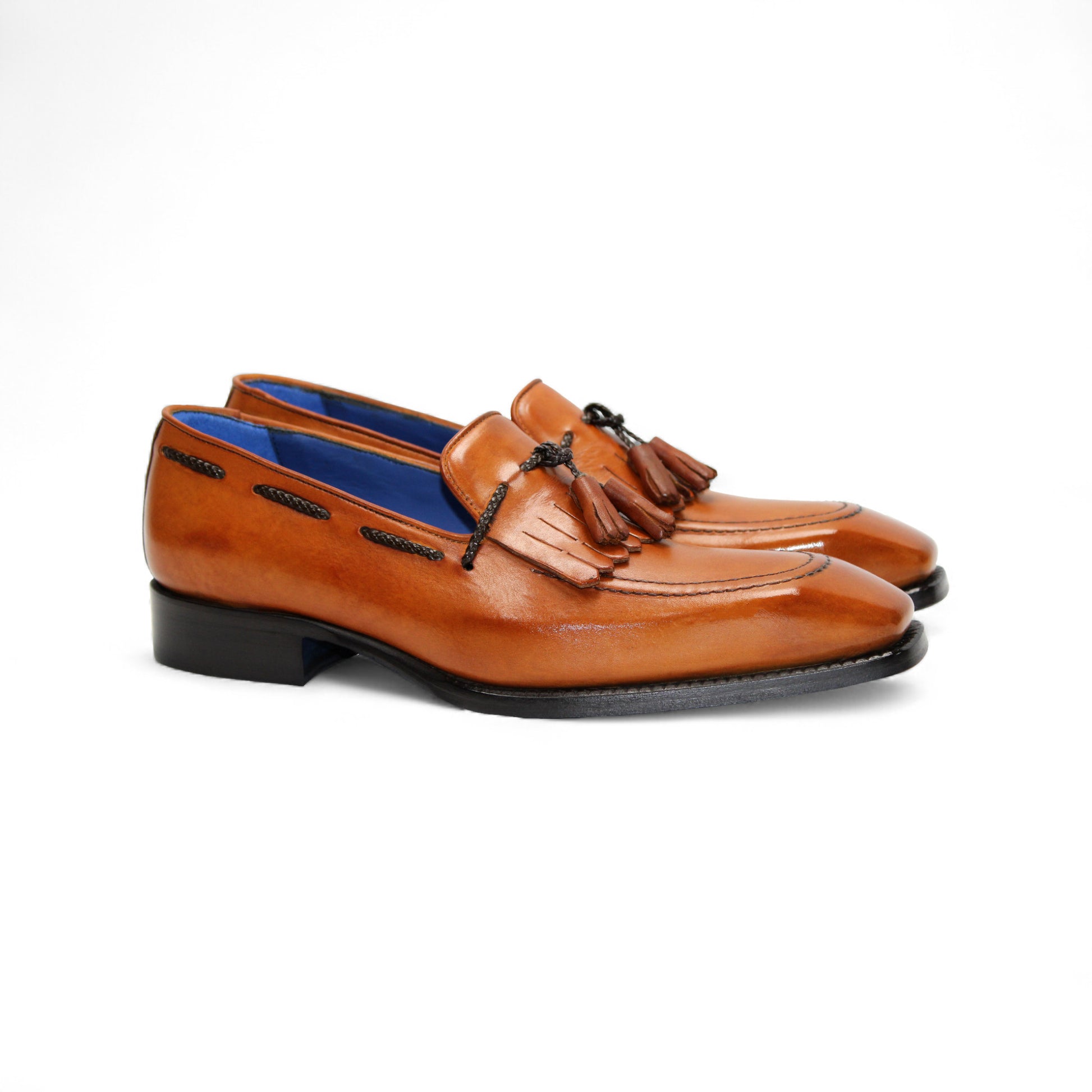 The Emilio Franco Tommaso Gold is a tan leather loafer with a tailored fit, low black heel, tassel detail on the upper, and dark side stitching, shown in side profile against a white background.