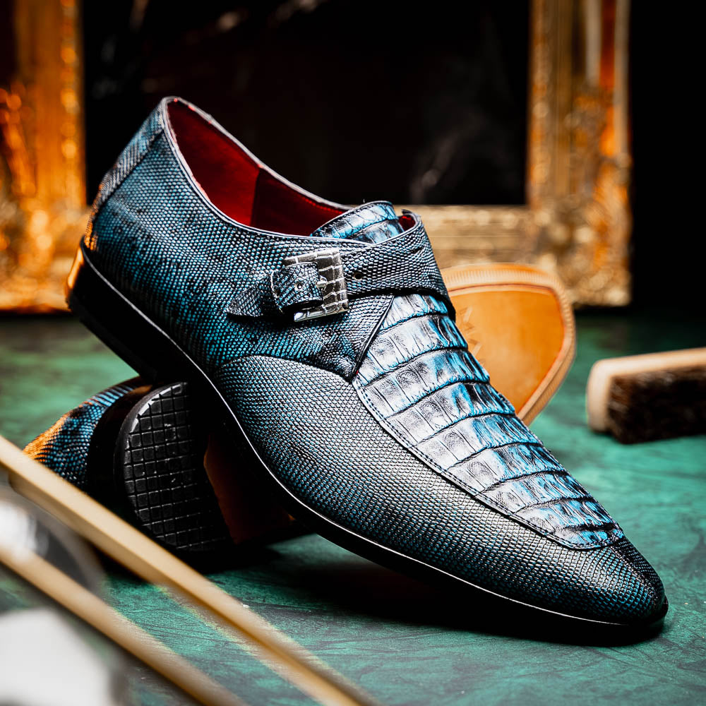 A pair of Toluca Rustic Blue exotic leather dress shoes by Marco Di Milano features a buckle detail, with one shoe on its side showing the tan leather sole and “MARCO DI MILANO” branding.