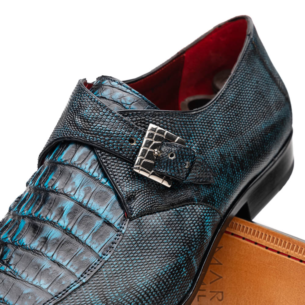 A pair of Toluca Rustic Blue exotic leather dress shoes by Marco Di Milano features a buckle detail, with one shoe on its side showing the tan leather sole and “MARCO DI MILANO” branding.