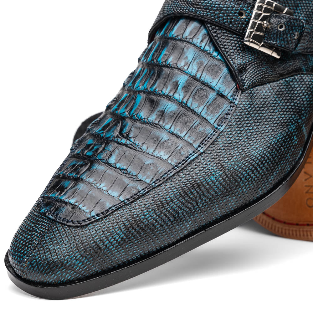 A pair of Toluca Rustic Blue exotic leather dress shoes by Marco Di Milano features a buckle detail, with one shoe on its side showing the tan leather sole and “MARCO DI MILANO” branding.