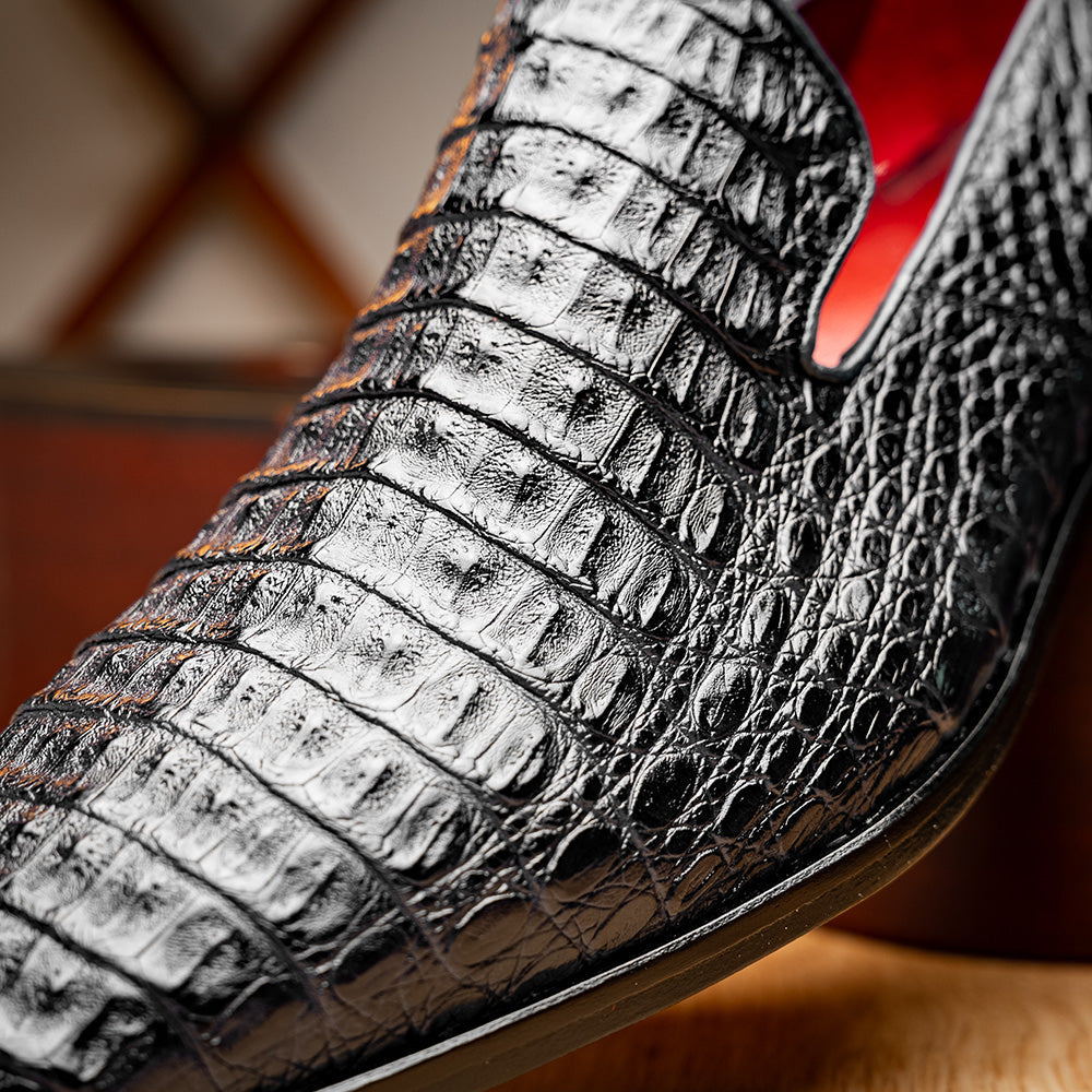 A pair of Marco Di Milano Trento Black loafers crafted from genuine caiman crocodile-pattern leather, showcasing a striking black exterior, red interior lining, and brown soles—one positioned upright and the other on its side. These luxury shoes feature exquisite hand-painted finishes for a truly sophisticated touch.