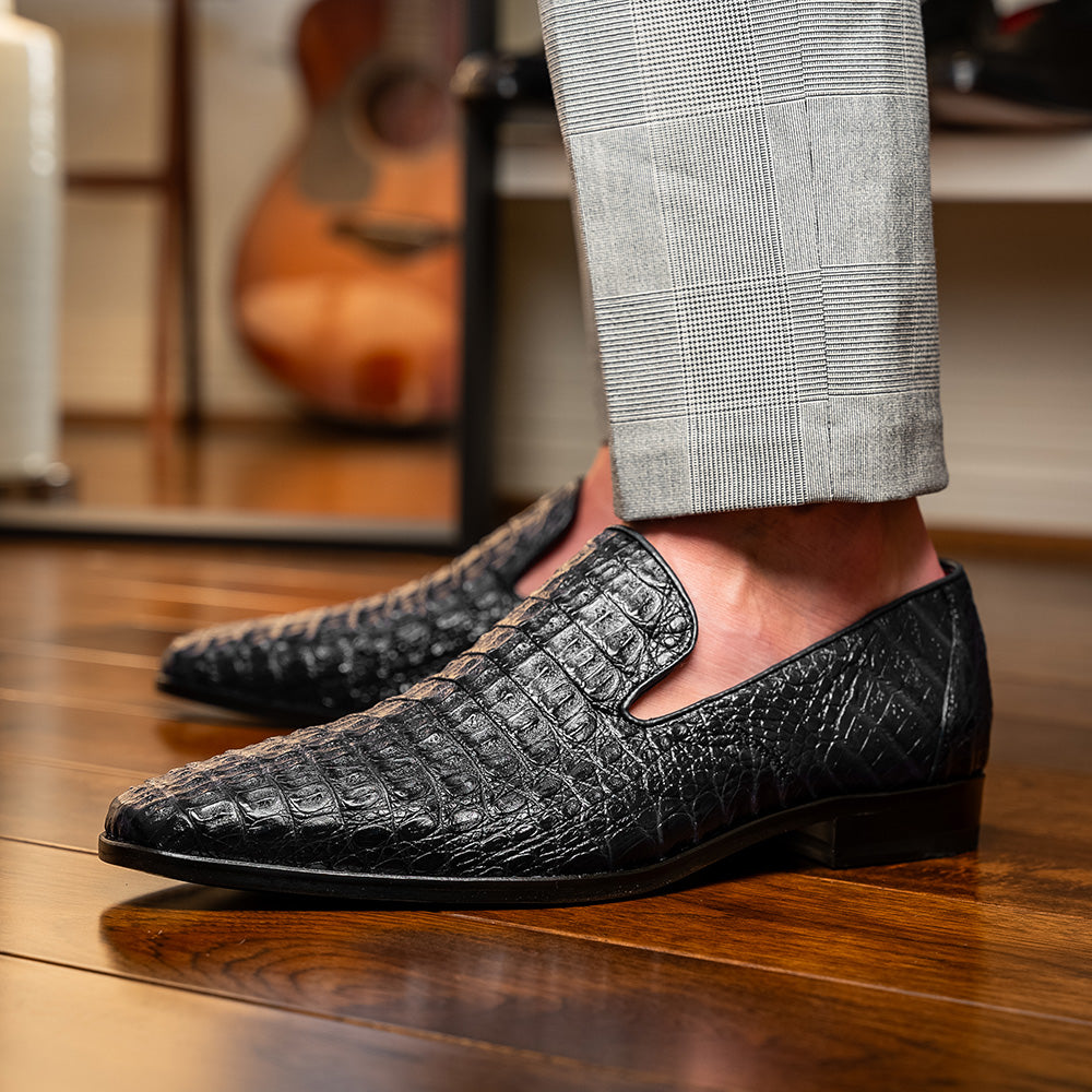 A pair of Marco Di Milano Trento Black loafers crafted from genuine caiman crocodile-pattern leather, showcasing a striking black exterior, red interior lining, and brown soles—one positioned upright and the other on its side. These luxury shoes feature exquisite hand-painted finishes for a truly sophisticated touch.
