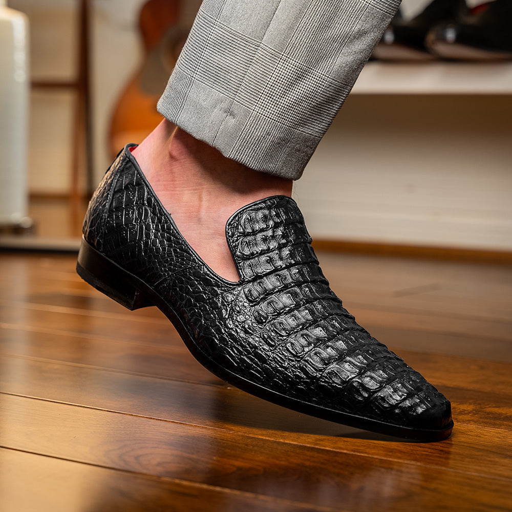 A pair of Marco Di Milano Trento Black loafers crafted from genuine caiman crocodile-pattern leather, showcasing a striking black exterior, red interior lining, and brown soles—one positioned upright and the other on its side. These luxury shoes feature exquisite hand-painted finishes for a truly sophisticated touch.