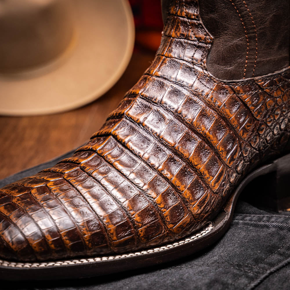 A pair of Marco Di Milano Tucson Aged Brown cowboy boots with textured caiman belly leather—one boot stands upright while the other displays its sole, branded "Marco di Milano.