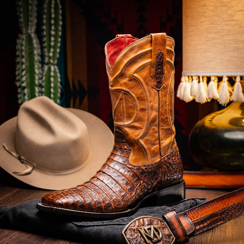 A pair of Tucson Aged Maple brown genuine leather western boots by Marco Di Milano with a textured finish; one boot upright, the other displaying the sole with "Marco Di Milano" branding.