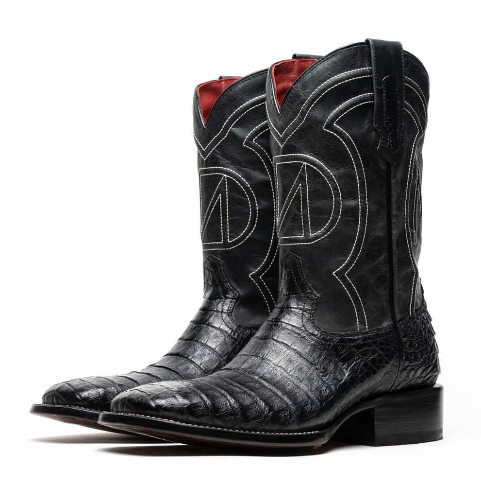 A pair of Tucson Black cowboy boots by Marco Di Milano; one boot stands upright highlighting the decorative stitching, while the other lies on its side showing the branded sole.