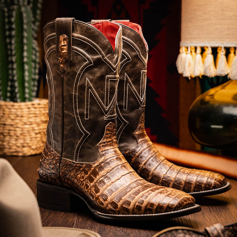 A pair of Tucson Stone Brown cowboy boots by Marco Di Milano, featuring brown leather with a reptile texture and square toe; one boot stands upright, the other displays its sole labeled with the brand.