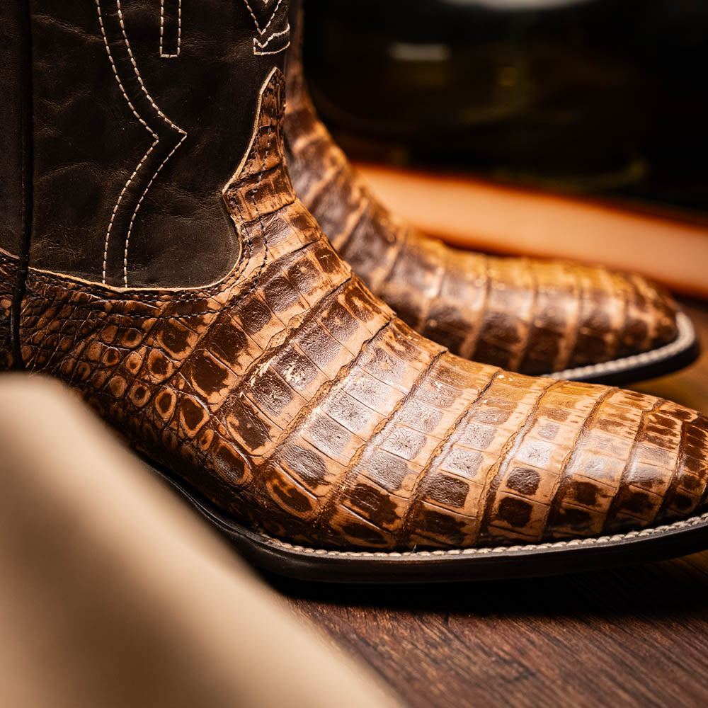 A pair of Tucson Stone Brown cowboy boots by Marco Di Milano, featuring brown leather with a reptile texture and square toe; one boot stands upright, the other displays its sole labeled with the brand.