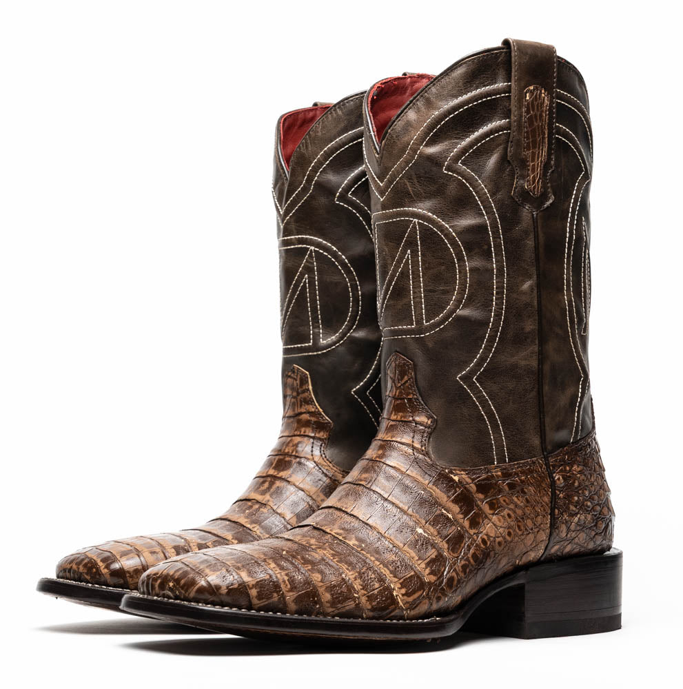 A pair of Tucson Stone Brown cowboy boots by Marco Di Milano, featuring brown leather with a reptile texture and square toe; one boot stands upright, the other displays its sole labeled with the brand.