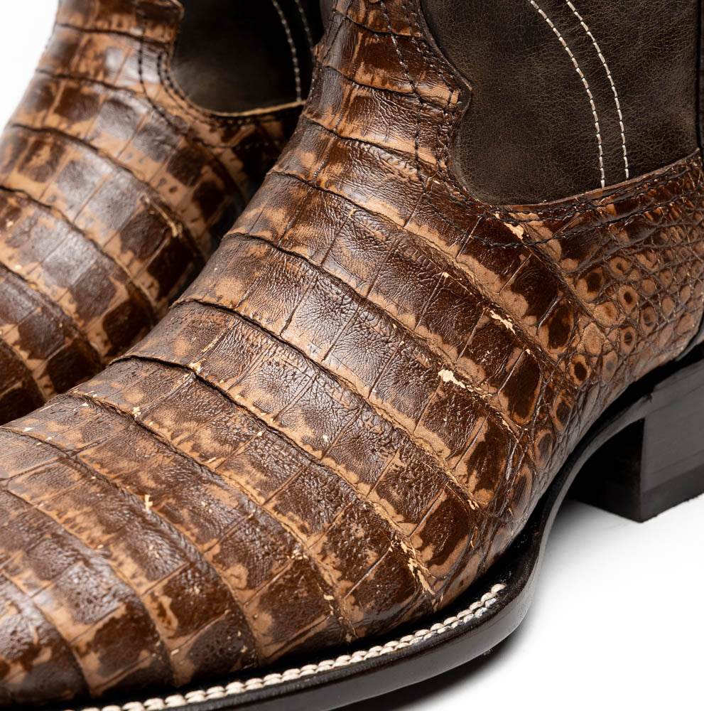 A pair of Tucson Stone Brown cowboy boots by Marco Di Milano, featuring brown leather with a reptile texture and square toe; one boot stands upright, the other displays its sole labeled with the brand.
