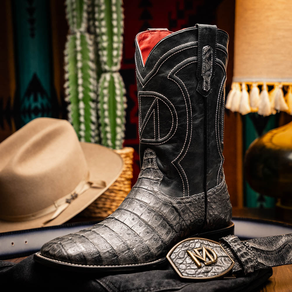 A pair of Tucson Stone Gray cowboy boots by Marco Di Milano with exotic textured leather, detailed white stitching, red inner lining, and the brand logo on the sole.